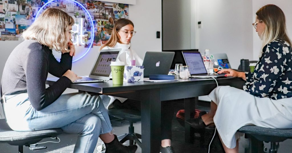 3 women sitting on chair in front of table with laptop computers