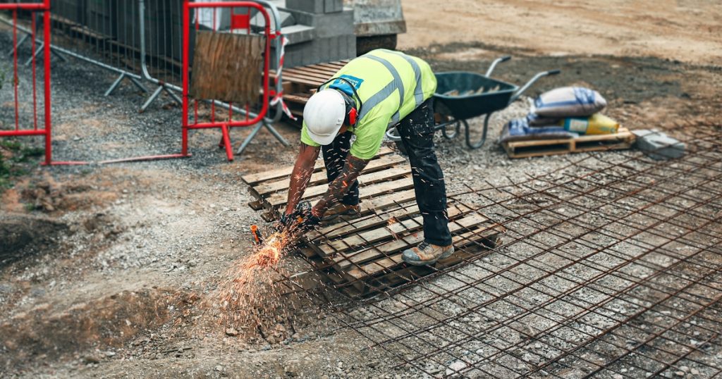 man in green and yellow safety vest and blue denim jeans standing on brown wooden pallet