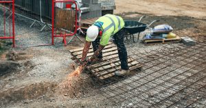man in green and yellow safety vest and blue denim jeans standing on brown wooden pallet