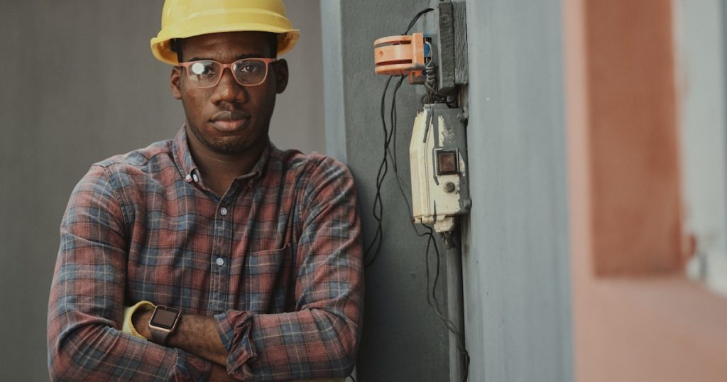 man in blue white and red plaid button up shirt wearing yellow hard hat holding black