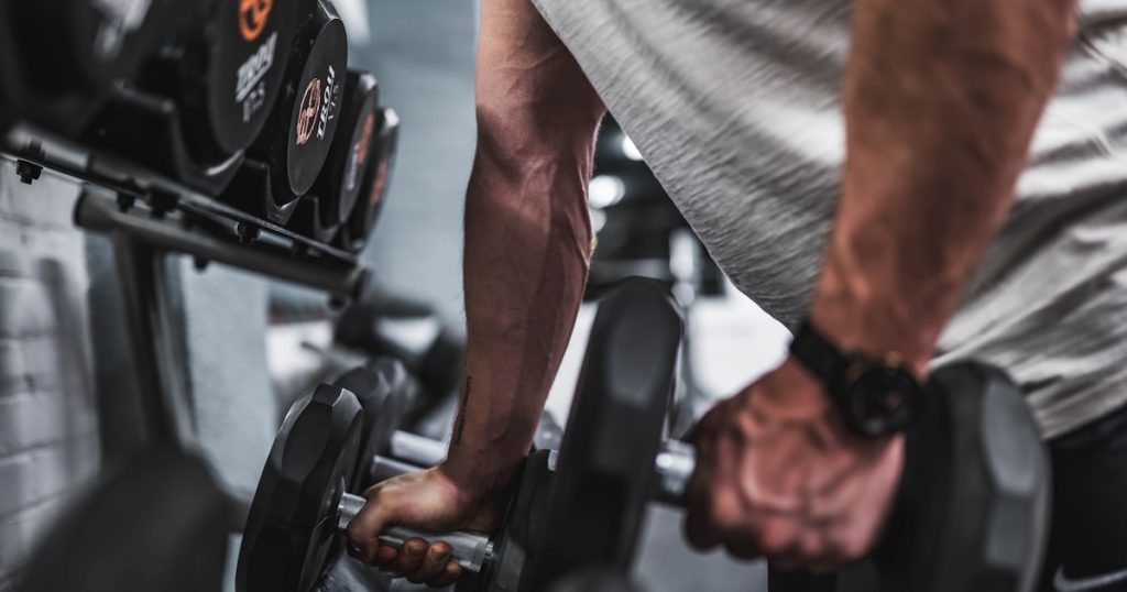 person in gray shirt holding black dumbbell