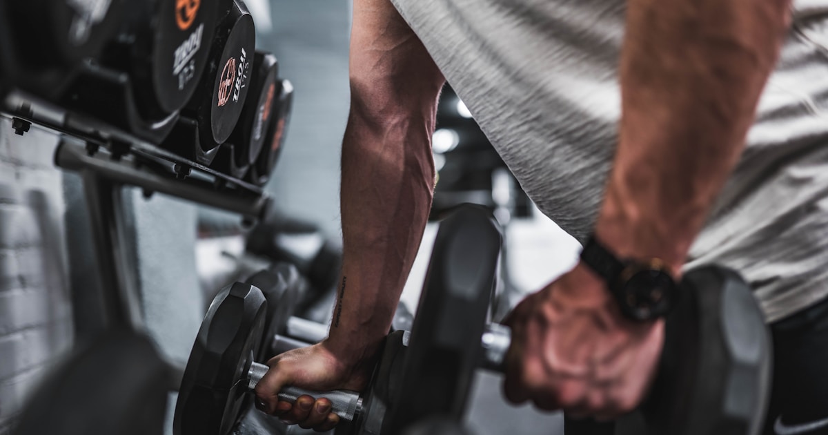 person in gray shirt holding black dumbbell