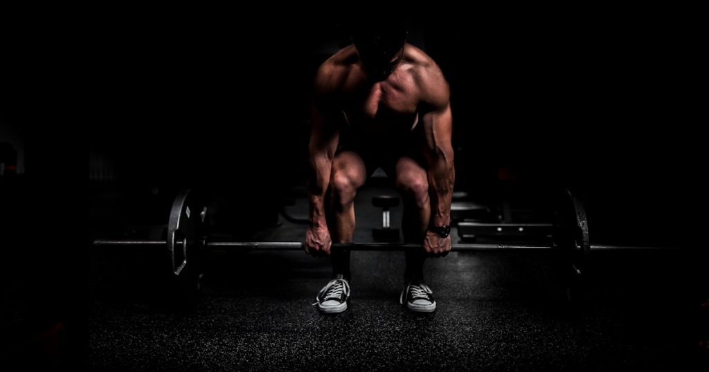 topless man in black shorts sitting on black and silver barbell
