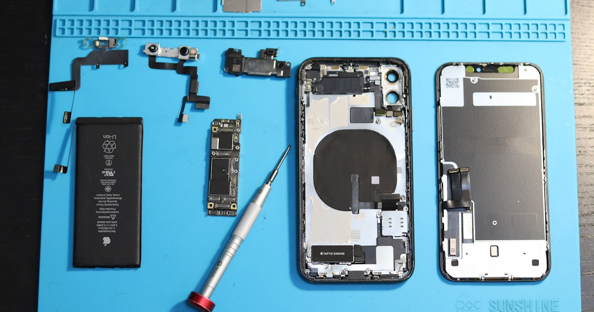 iPhone components are disassembled on a blue mat.