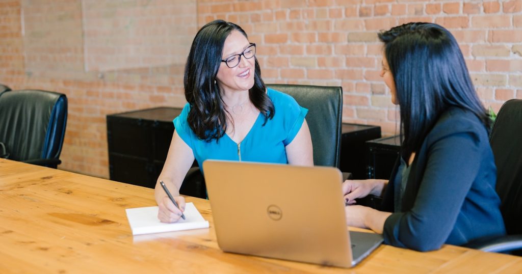 woman in teal t-shirt sitting beside woman in suit jacket