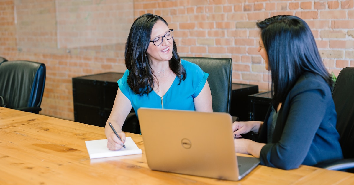 woman in teal t-shirt sitting beside woman in suit jacket