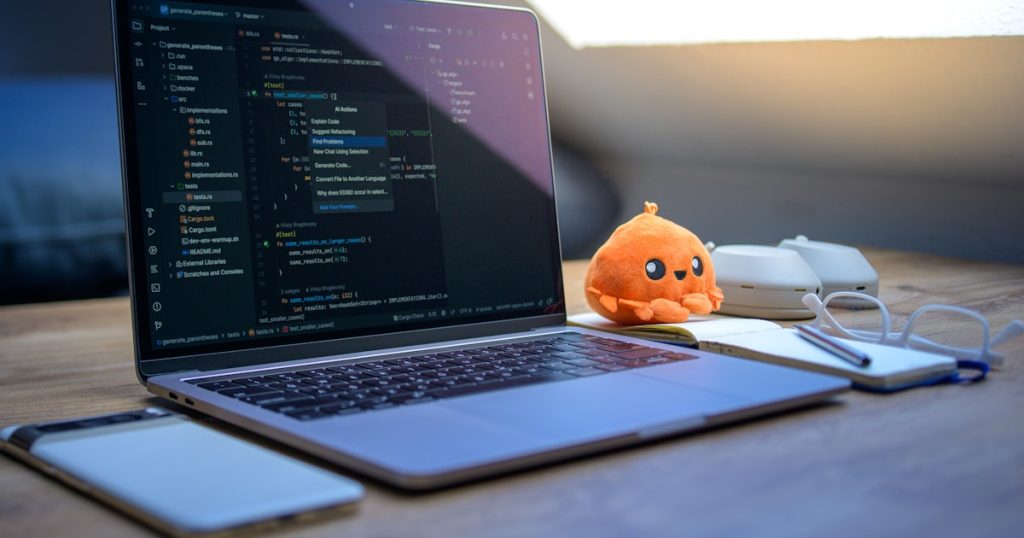 Laptop with code, phone, glasses, and plush toy.