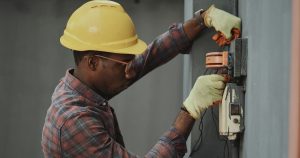 man in brown and white plaid dress shirt and yellow hard hat holding black and orange