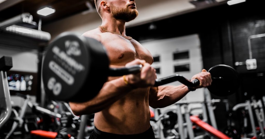 topless man in black shorts carrying black dumbbell