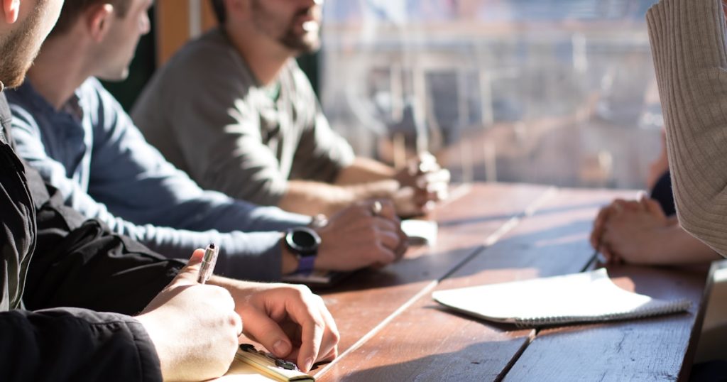 people sitting on chair in front of table while holding pens during daytime