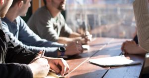 people sitting on chair in front of table while holding pens during daytime