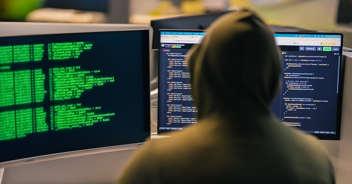 Hacker in hoodie working on multiple computer screens