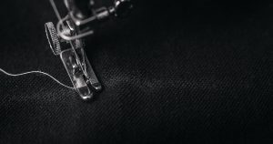 photo of gray sewing machine foot lock with thread on black cloth