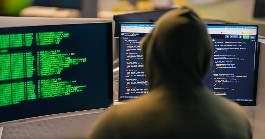 Hacker in hoodie working on multiple computer screens