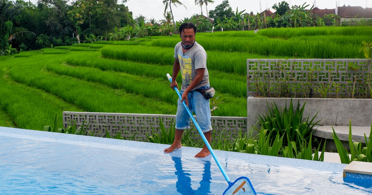 man in white polo shirt and blue denim jeans standing on swimming pool during daytime
