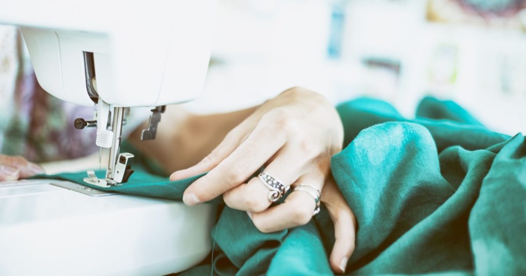 person sewing green textile using white electric sewing machine