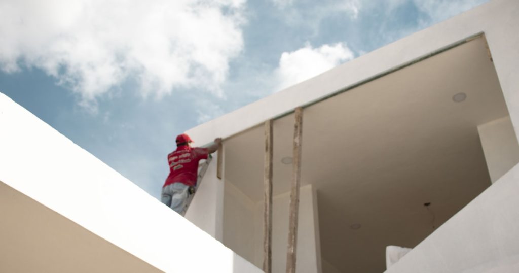man in red jacket standing on white concrete building under blue and white cloudy sky during