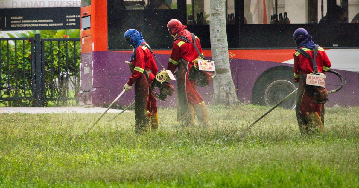 man in red jacket holding a stick near red bus during daytime